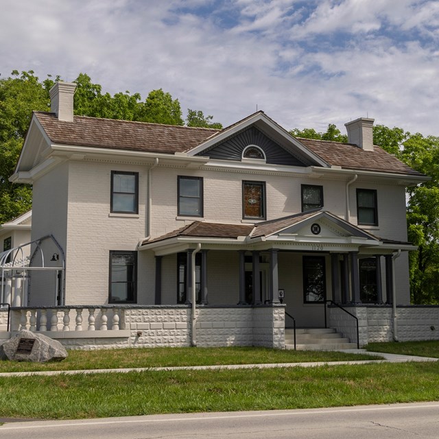A large two-story house with five windows in a row on each level and a peaked roof in center.