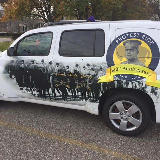 A car with wrapped artwork showing several mounted soldiers and portrait of Charles Young in circle