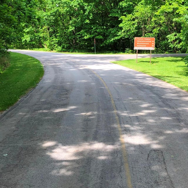 A two-lane road curves to the left with a directional sign on the right side of the road