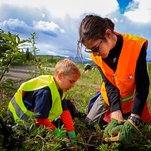 two children in safety vests pull weeds