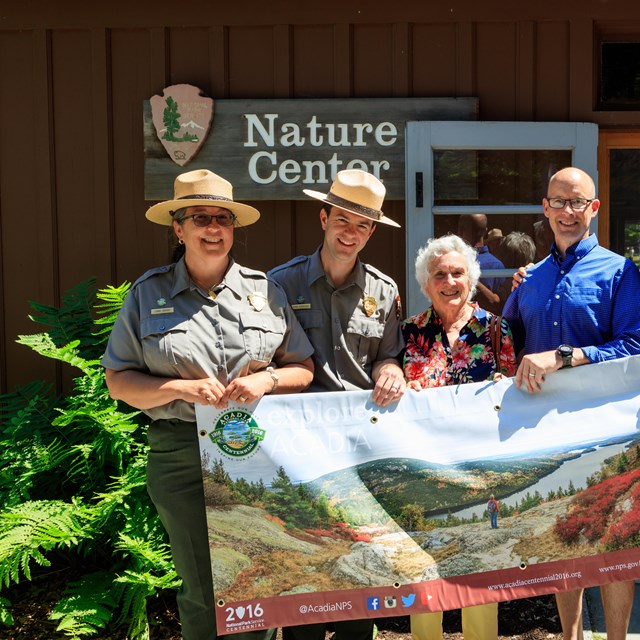 seven people hold up a banner in front of nature center