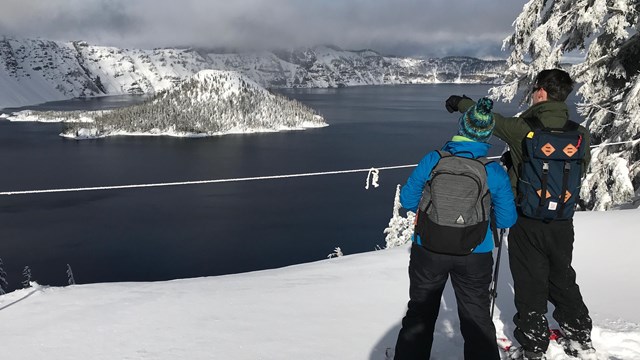 Snowshoers view the lake from behind a rope which indicates the rim edge