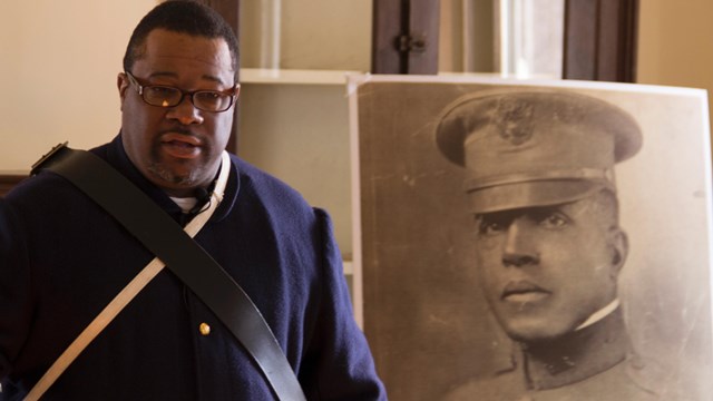 Living historian in Buffalo soldiers uniform in front of portrait of Charles Young