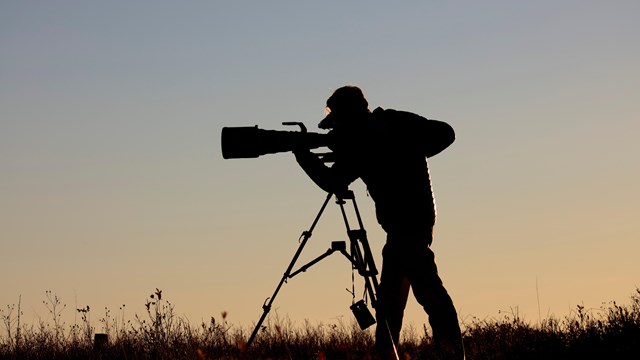 Silhouette of photographer with large lens camera