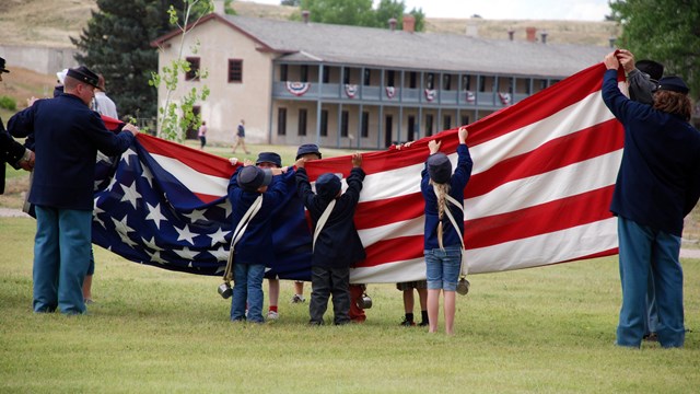 19th-century military reenactors and kids folding a large US flag