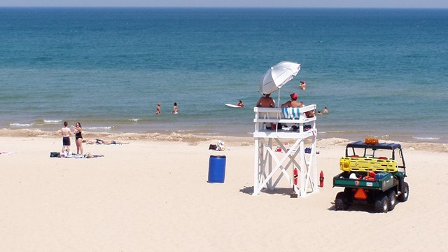 Lifeguard stand and vehicle on beach near people walking and swimming