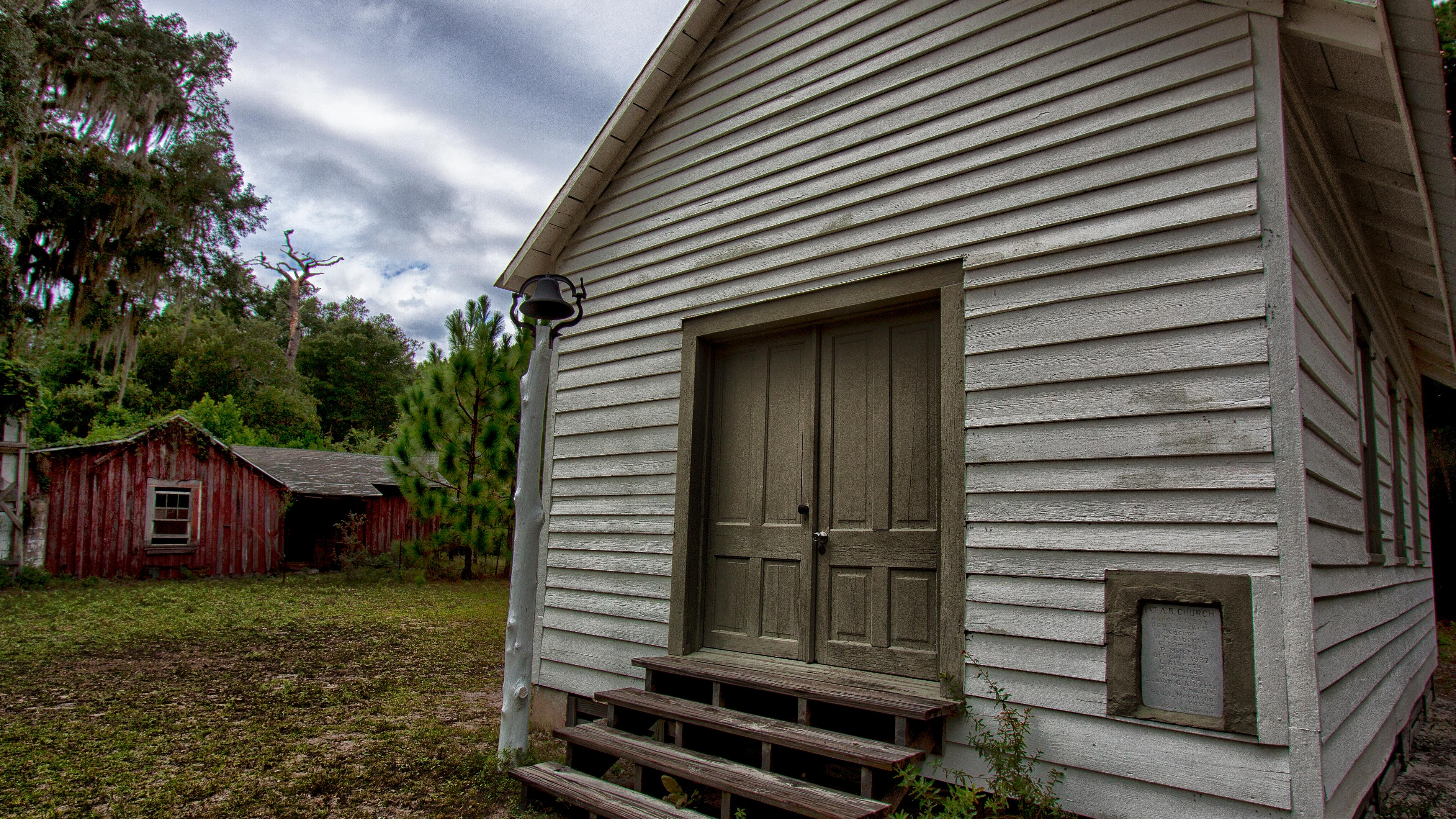 One room white church with a red rundown house in the back