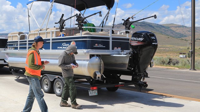 Two people approach a trailered motorboat to conduct an inspection