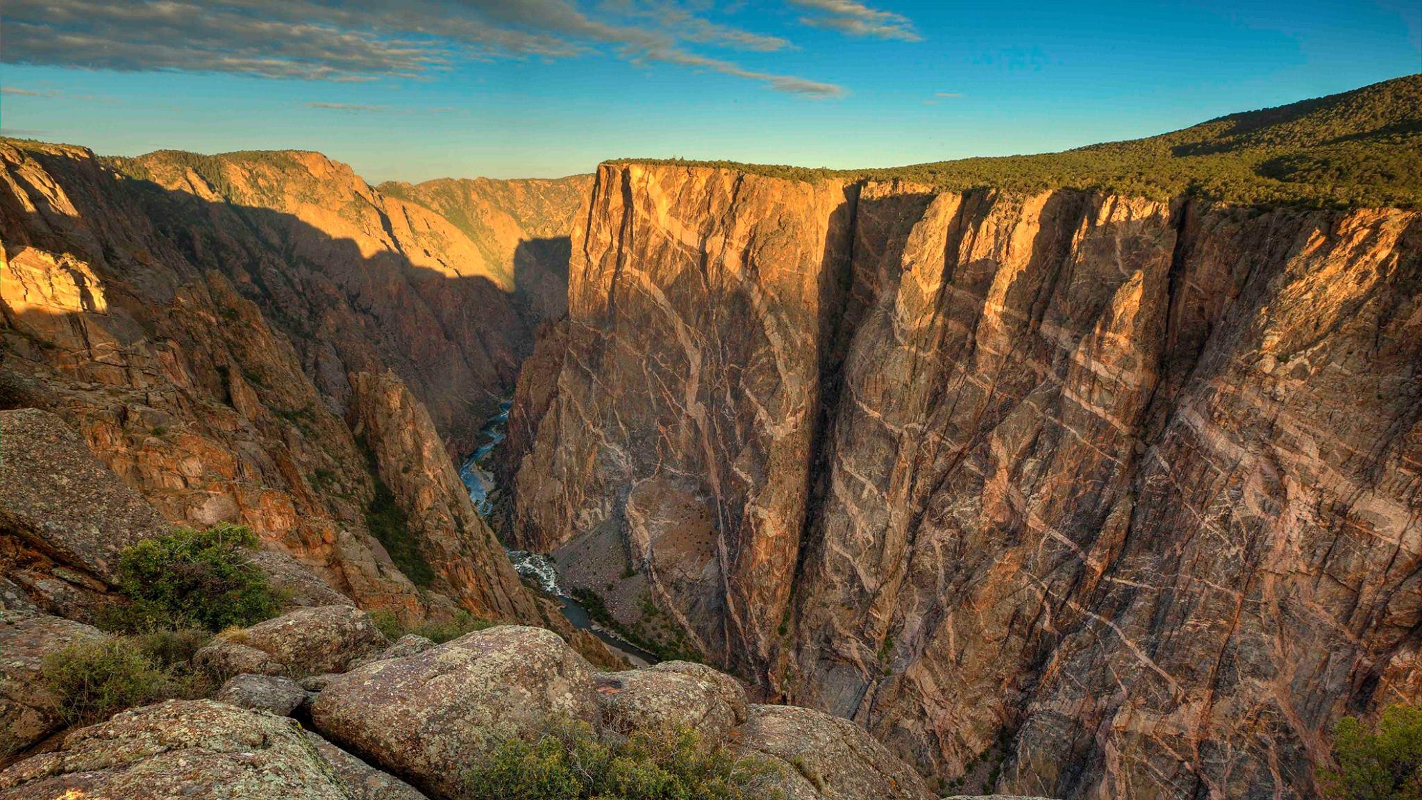 Sunset light hits a canyon wall and illuminates various colored intrusions in the rock