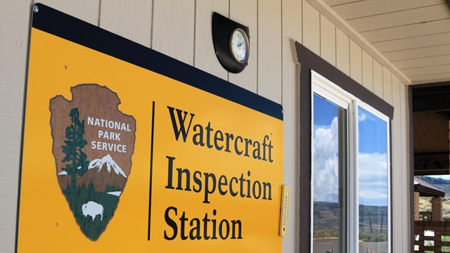 A yellow sign with 'Watercraft Inspection Station' and an NPS arrowhead.