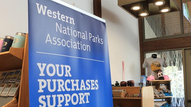 A large blue banner with 'Your Purchases Support Parks' in front of bookshelves with items