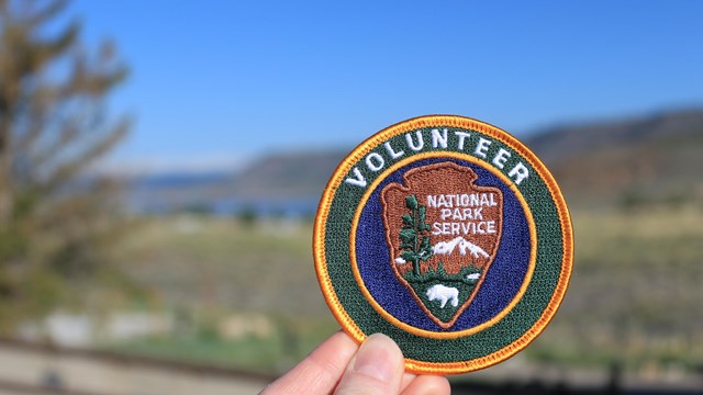 A circle patch with a National Park Service volunteer logo being held up