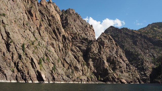 Tall, dark canyon walls with water at the base. A blue sky with clouds is above the canyon.