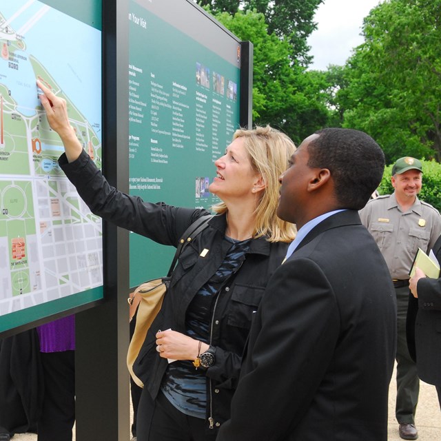 A woman points on a large outdoor map.