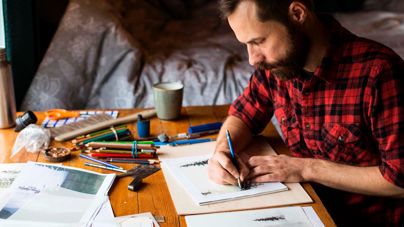 man sitting at a table drawing in a sketchbook