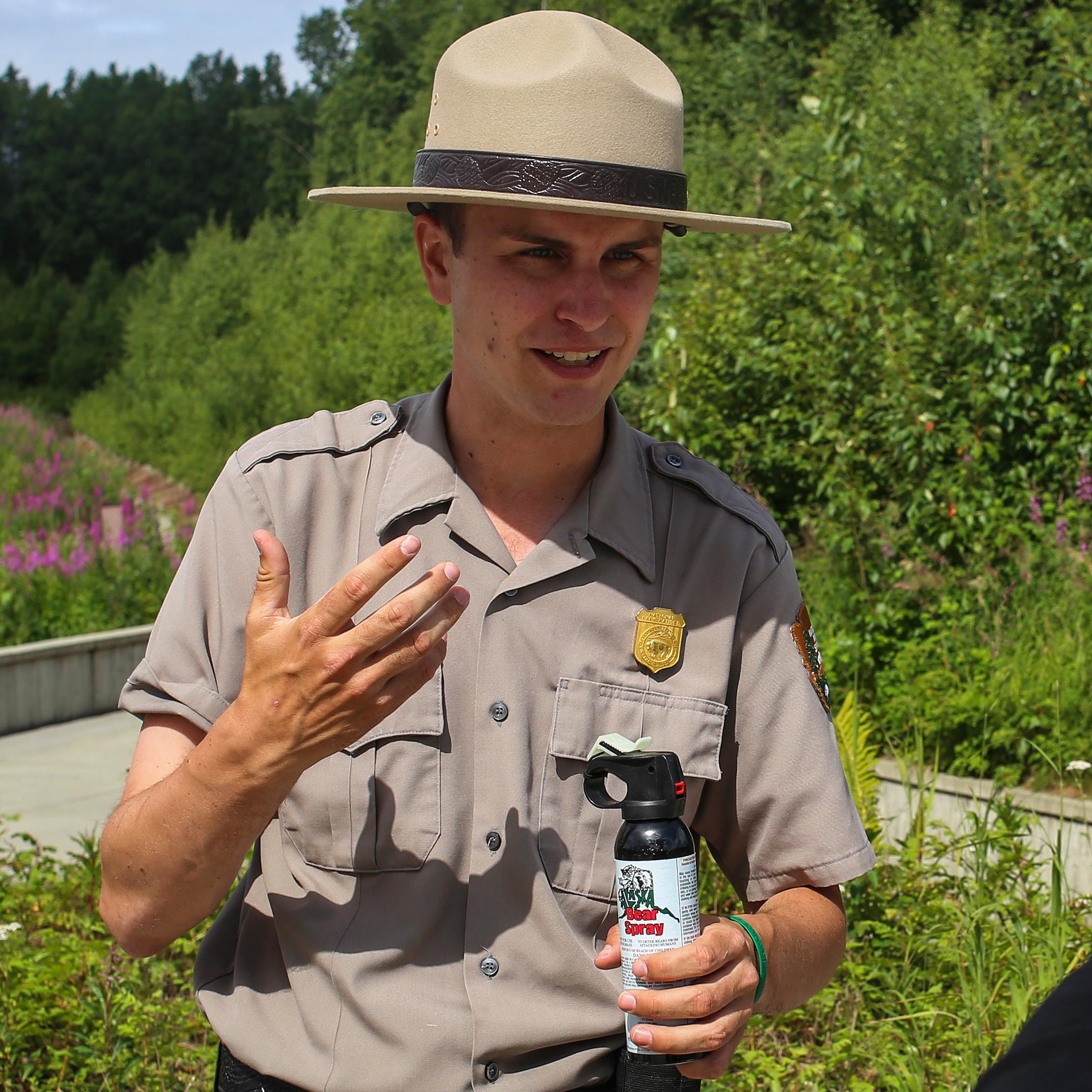 A park ranger holds a can of bear spray and talks to a woman.