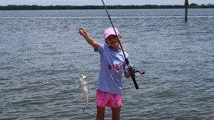 Young Girl holds fish she has caught with the Manatee River in the background