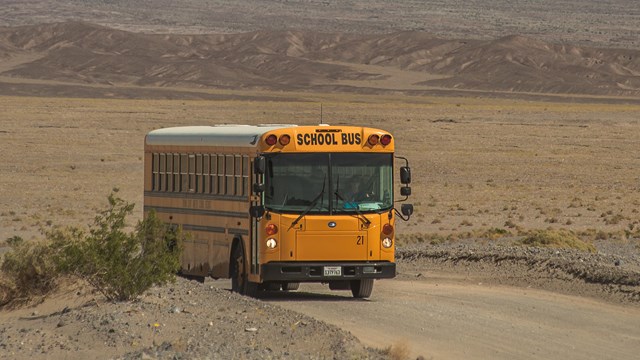 A bus drives on a road with a mountain range in the background.
