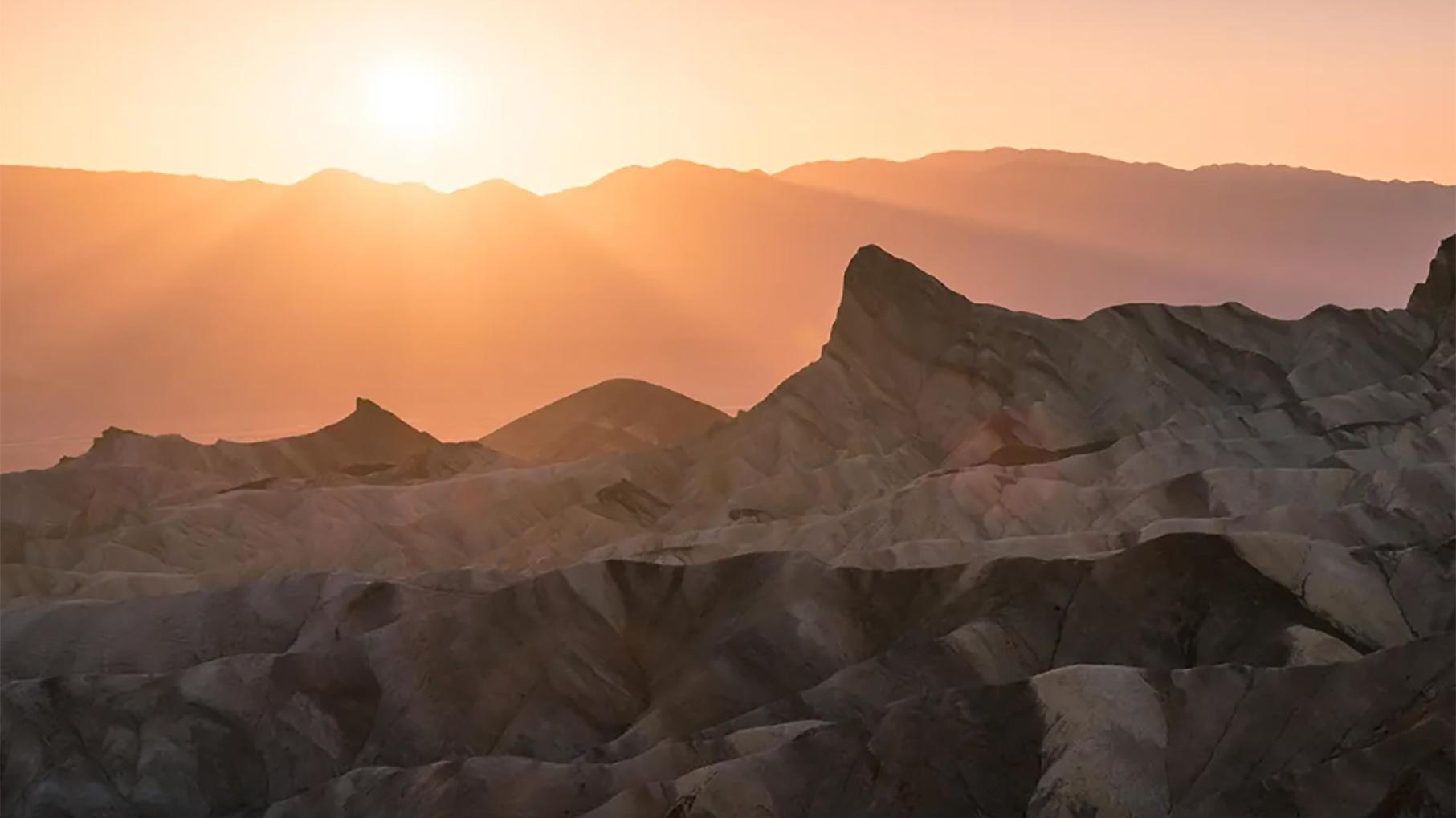 The warm pink and gold light of sunset covers beige badlands.