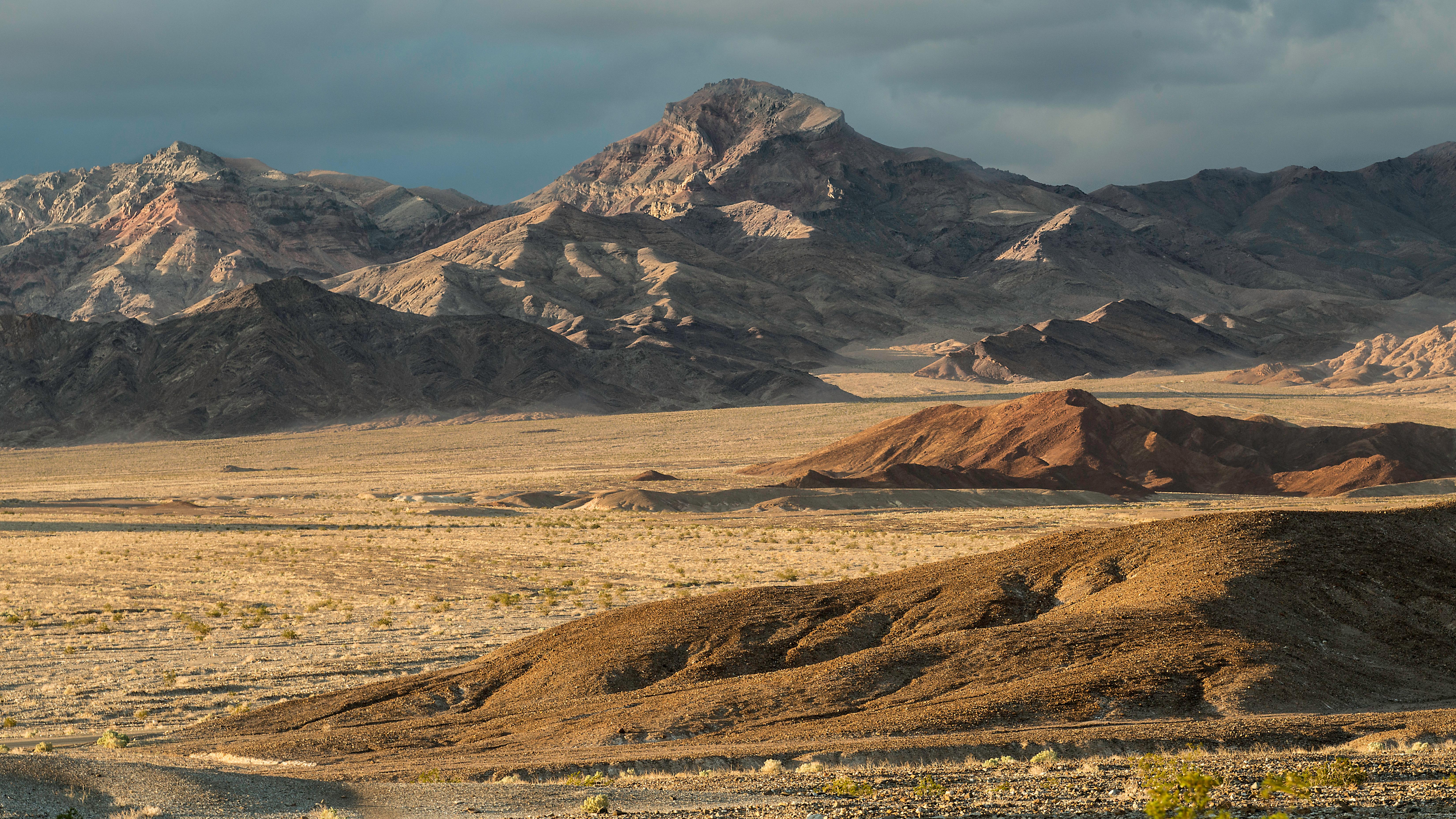 A barren desert stretches across layered ground toward a wall of jagged mountains.