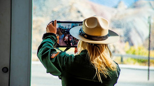 A ranger holds a tablet up to a window to show the landscape to the students on screen.