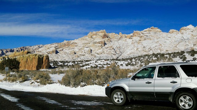 Silver vehicle sitting on road with rocky mountains covered in snow in the background