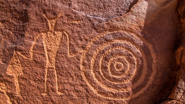 Rock etchings featuring a human figure next to a pattern of concentric circles.