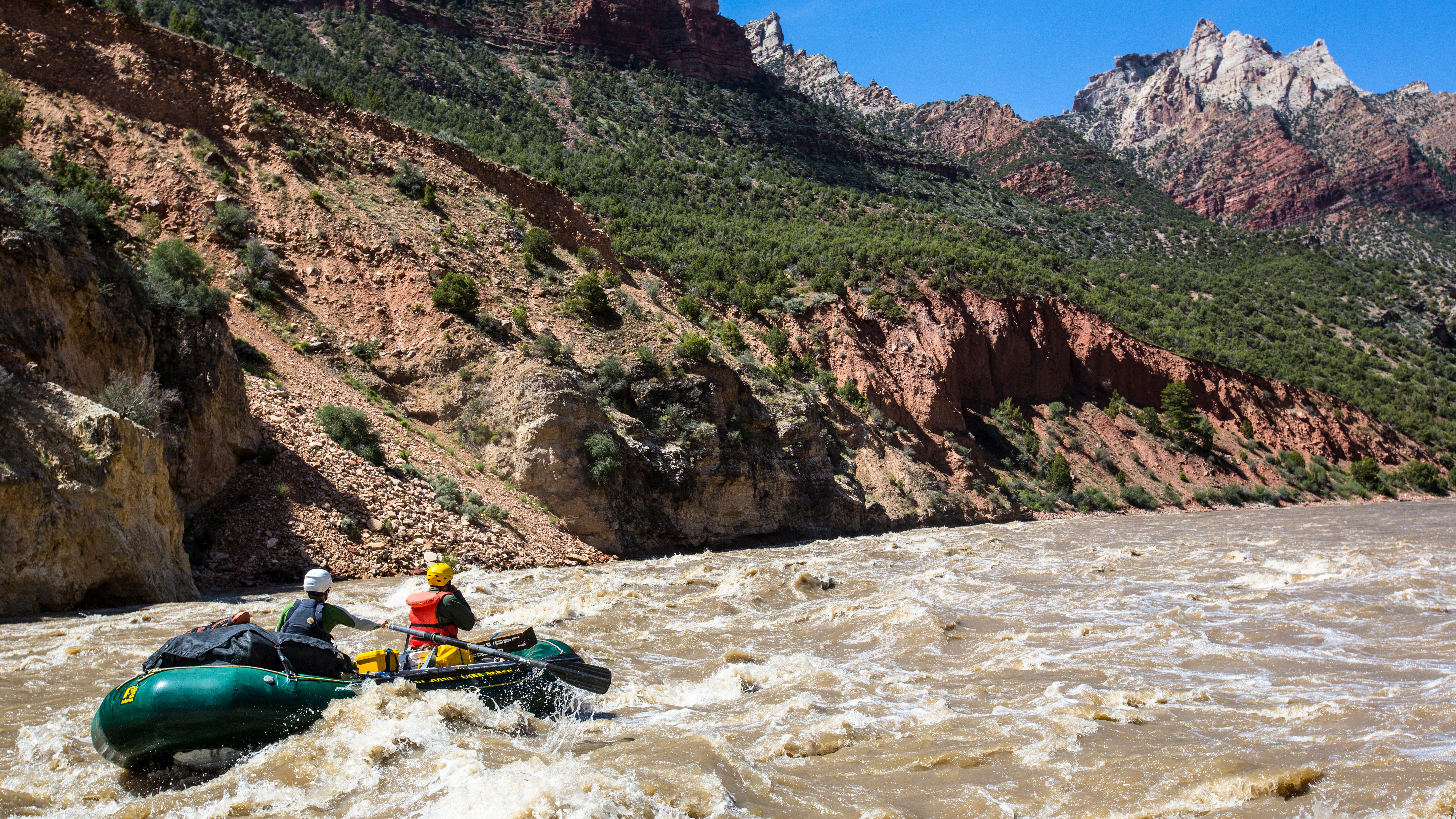 A green raft crashes through a wave in a rapid.