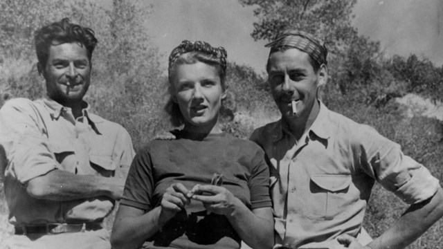 A black and white photo of a woman standing between two men.