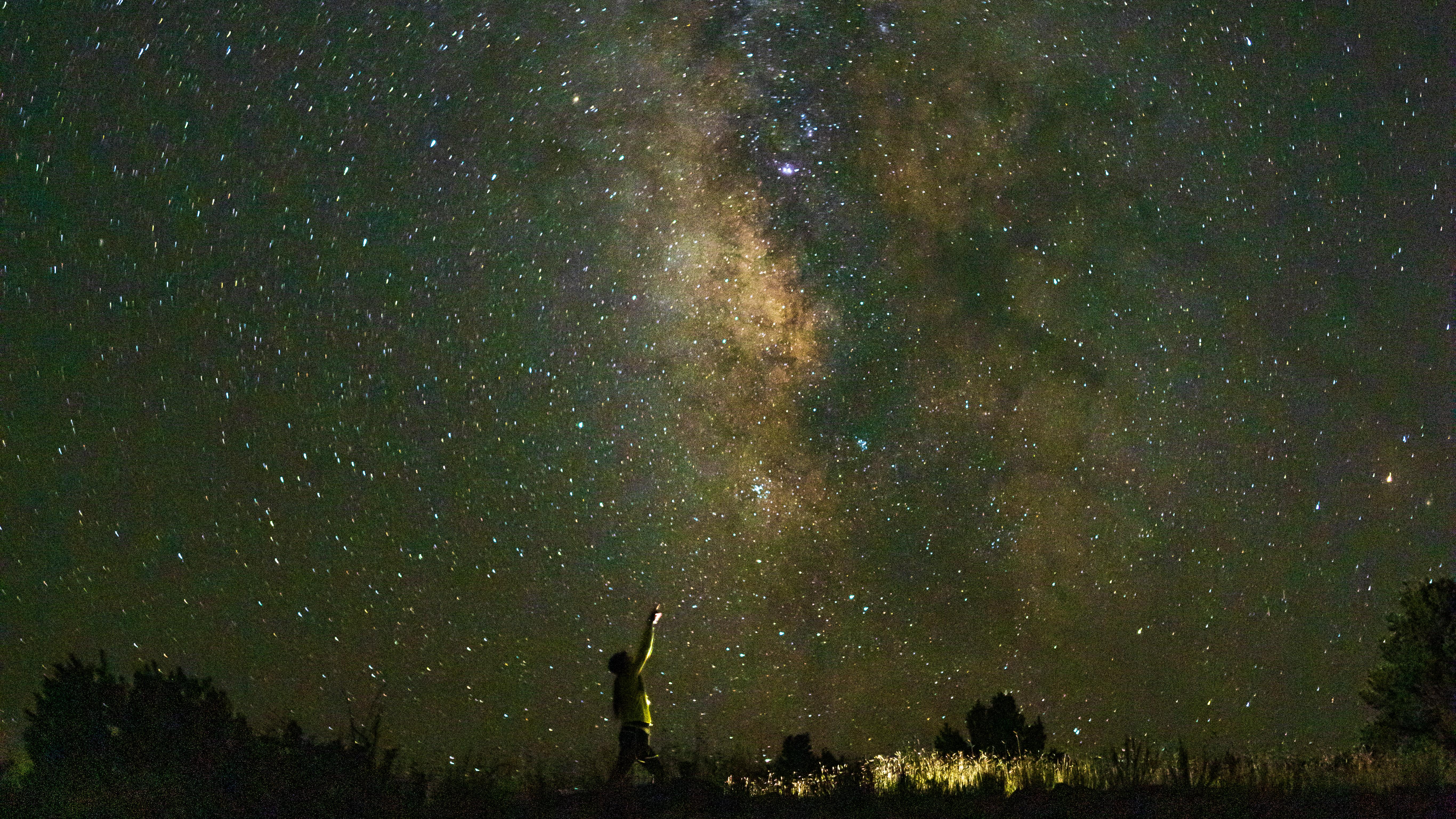 A person lit by a flashlight points up at the Milky Way galaxy above