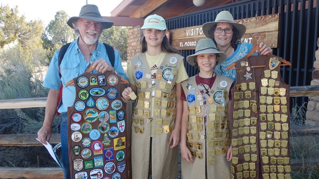 Two adults and two children display hundreds of Junior Ranger badges in the visitor center.