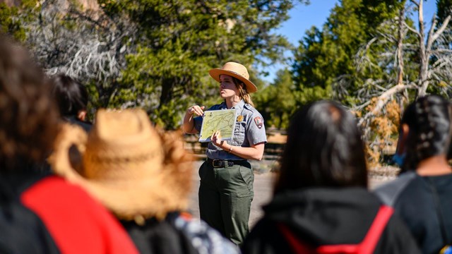A ranger showing a map to a group of children in front of the sandstone bluff.