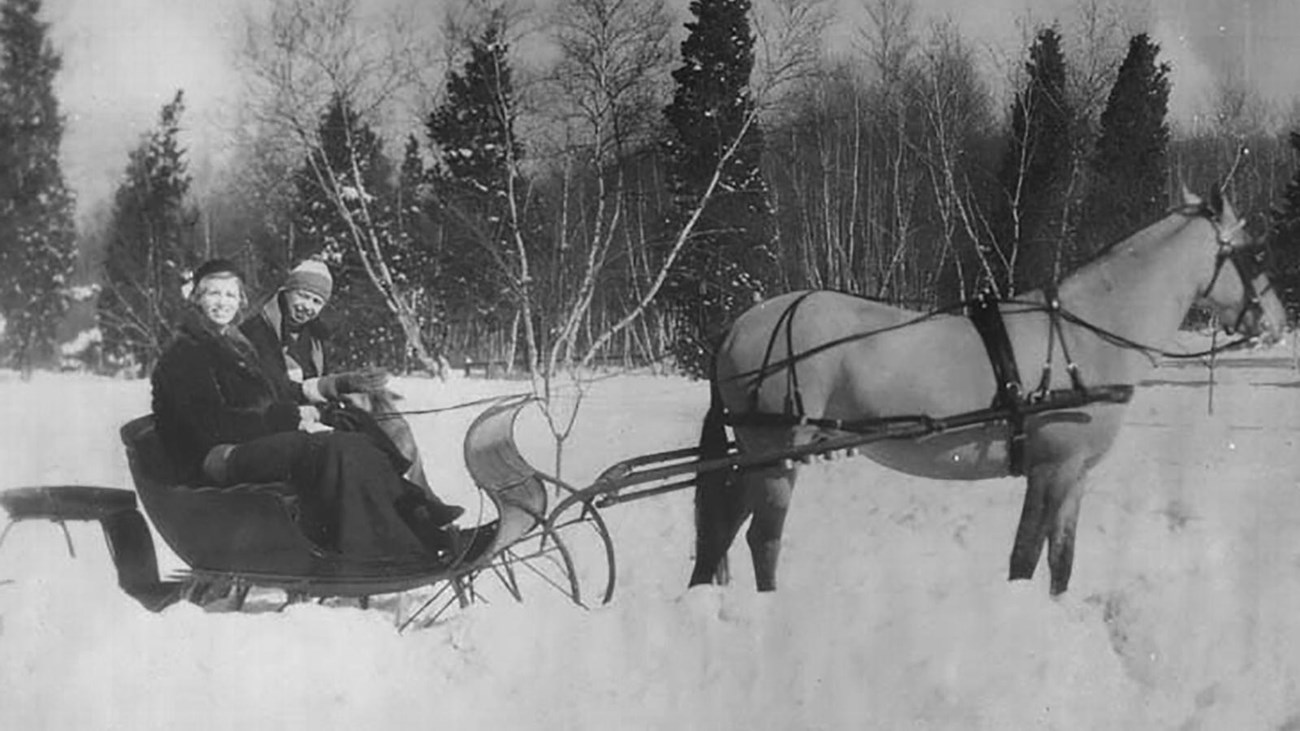 Two women in a horse drawn sleigh on a snowy landscape.