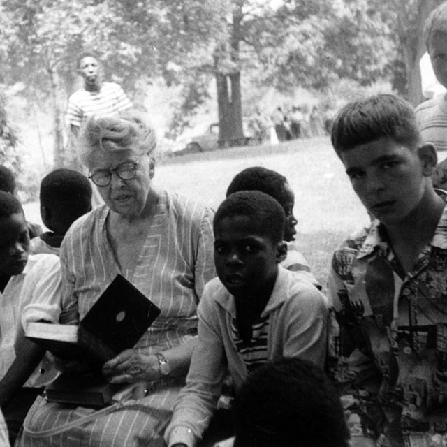 A woman reading to a group of children outdoors.