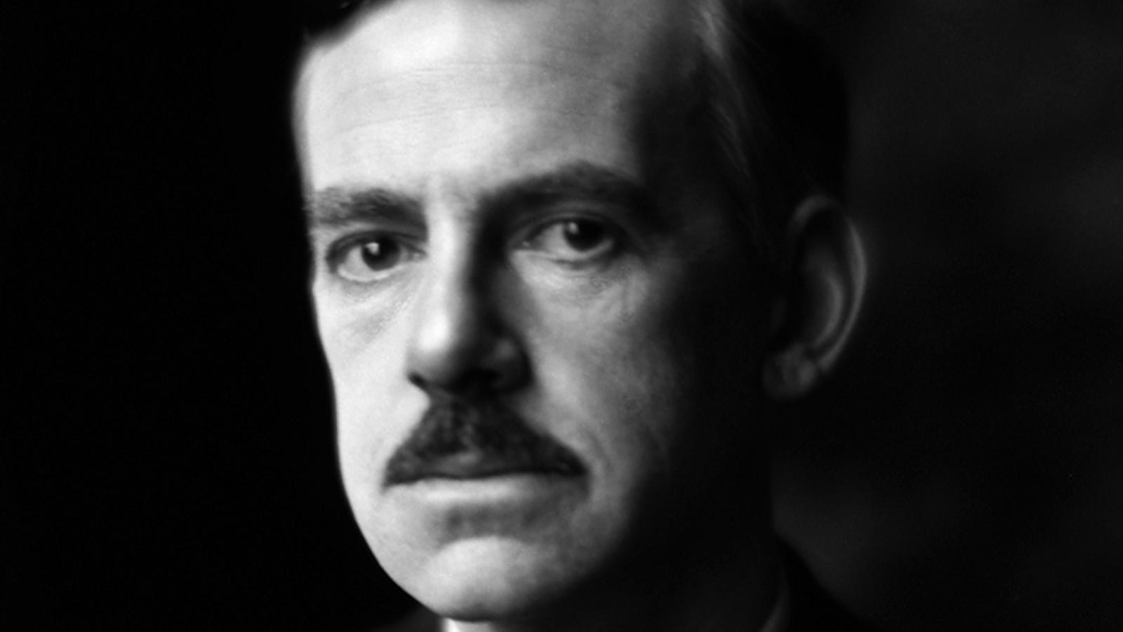 Black-and-white portrait of a man with a mustache, gazing intently at the camera. 
