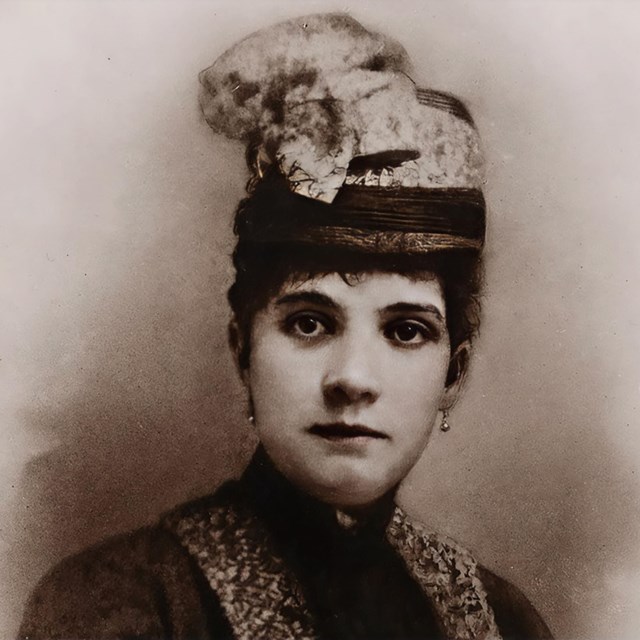 An elegant woman is wearing a hat and dress while posing for the camera. 