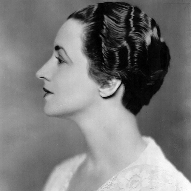 An elegant woman poses for a publicity photo with a side profile. She's wearing a simple dress.