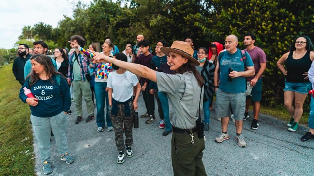 A Park Ranger leads a program for a large group of people. The ranger points.