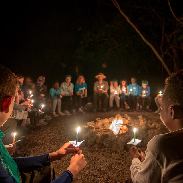 Students holding candles around a campfire.