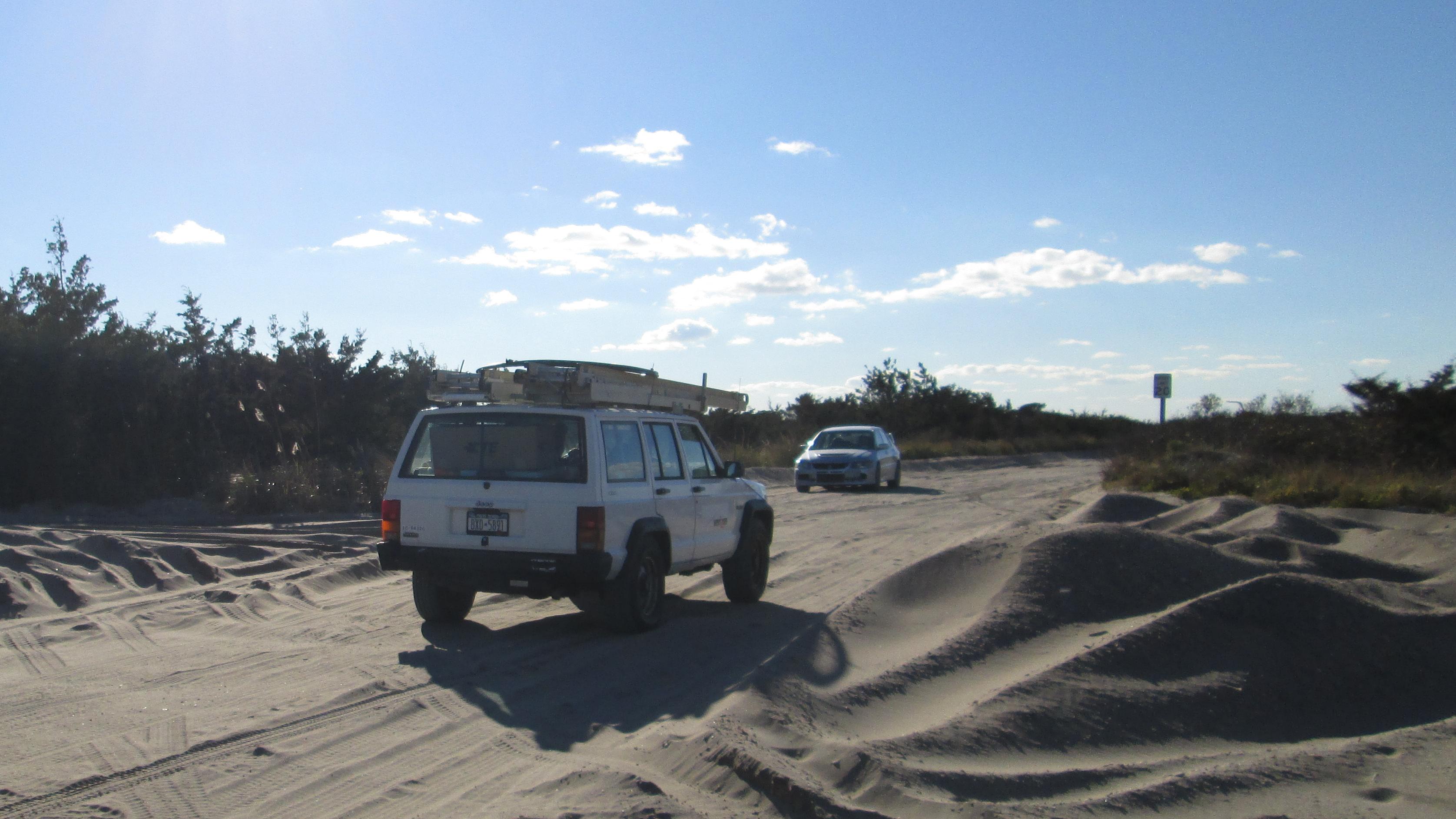 Two vehicles drive on a sand road.