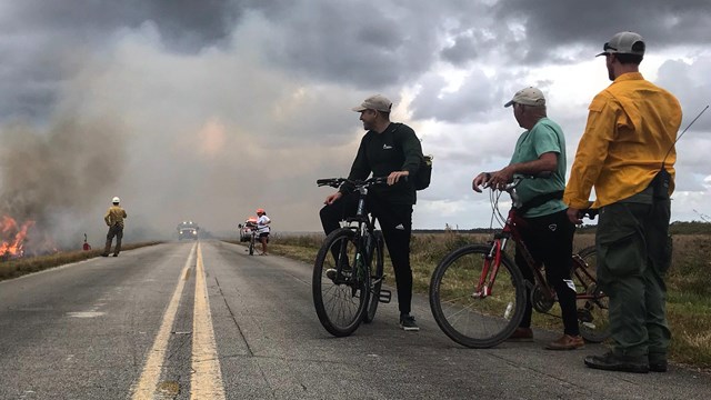 Two bicyclists stop along the road to talk to a wildland firefighter.