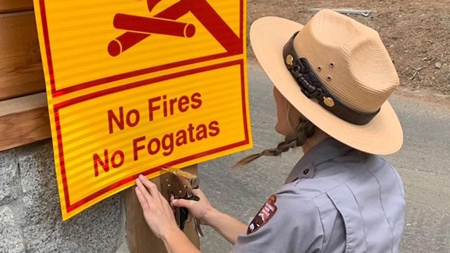 Park ranger hangs a sign that says no fires.