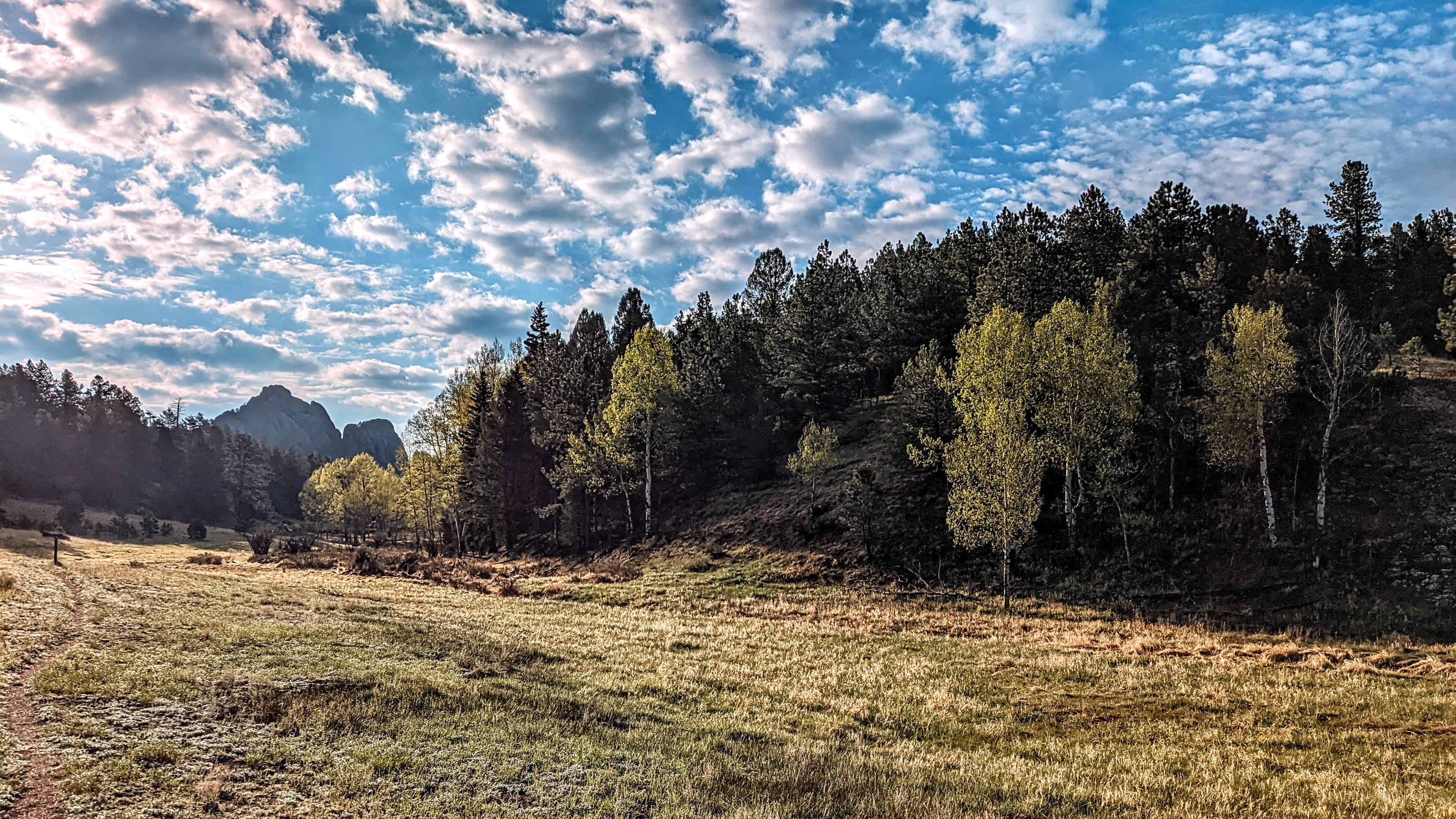A trail winds through a valley under a cloudy sky with a large rock formation in the background.