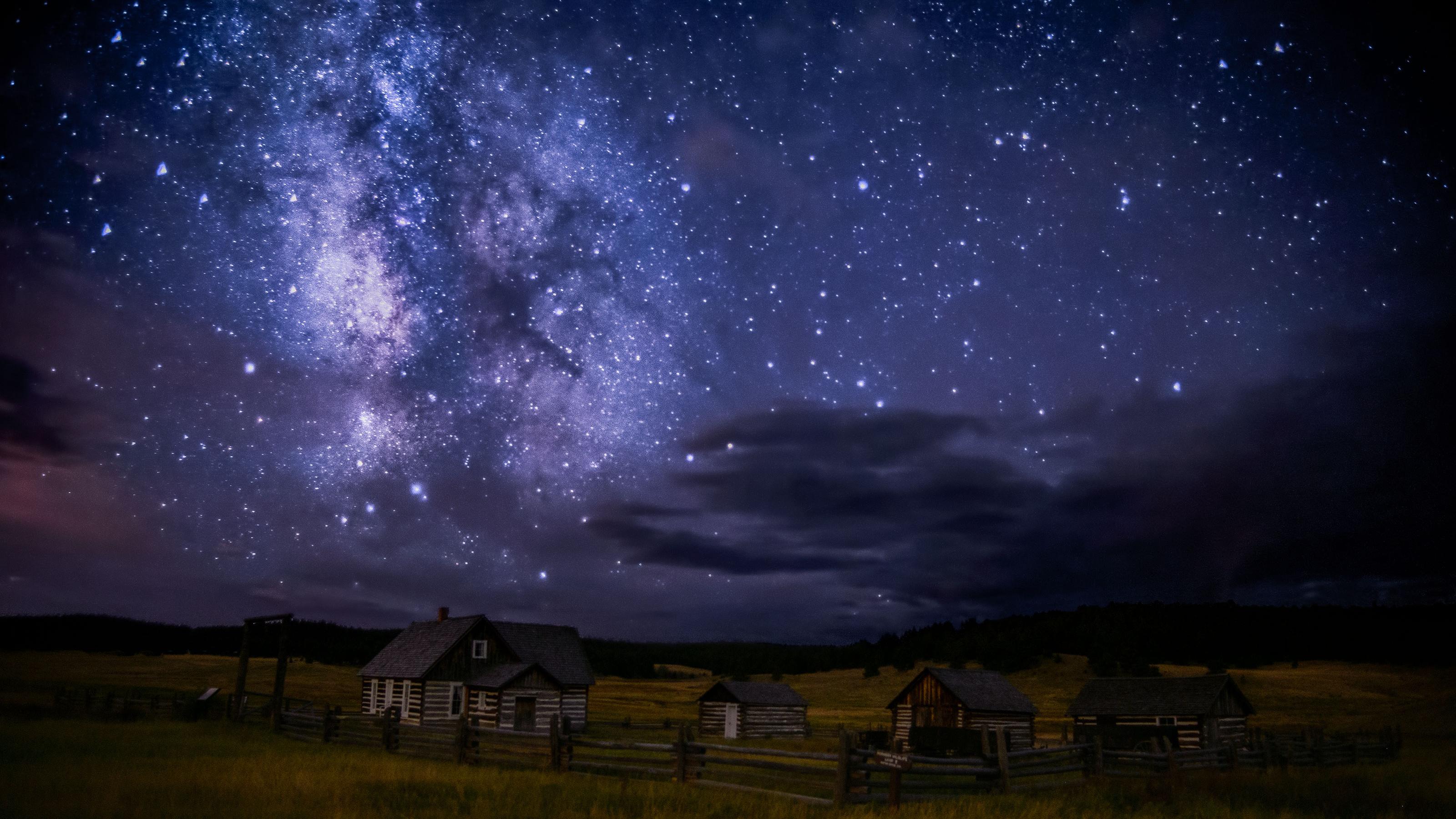 A star filled sky twinkles above a historic cabin and outbuildings.