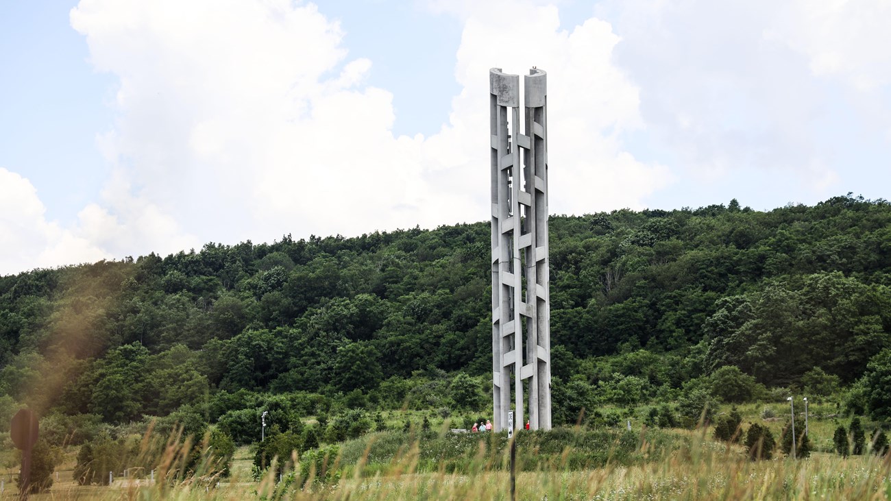 A trail leads to the Tower of Voices. Wildflowers and conifer trees surrounding the tower.