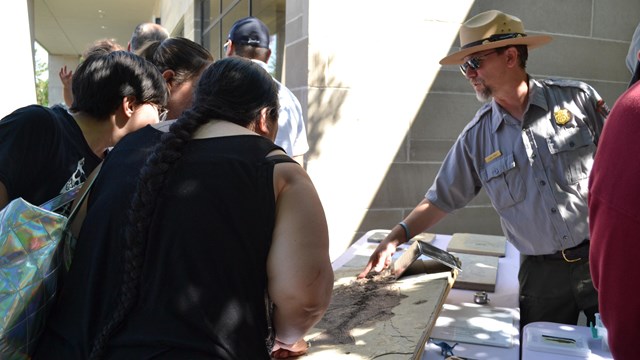 A ranger talking to three people points at a large fossil fish on a table.