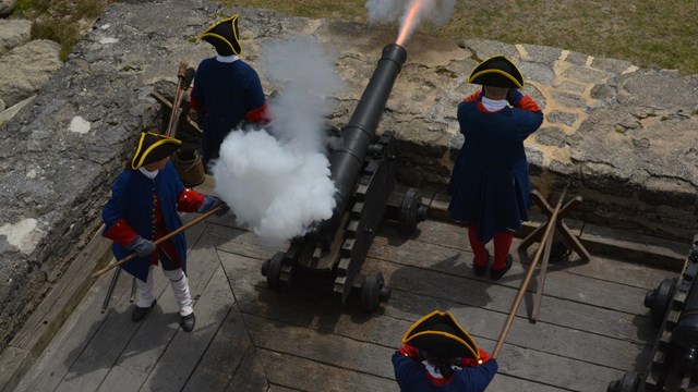 Cannon being fired surrounded by four soldiers. 