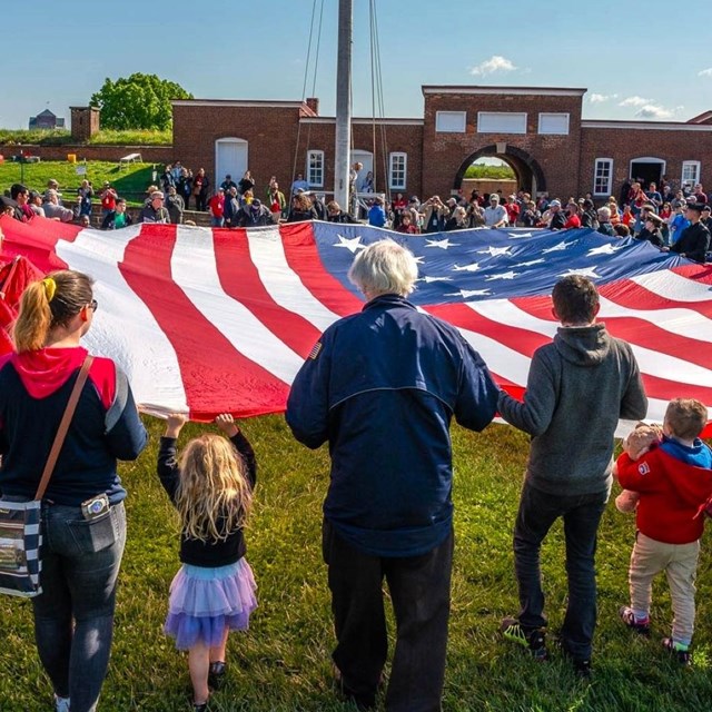 Large group of visitors assisting with folding a large American flag