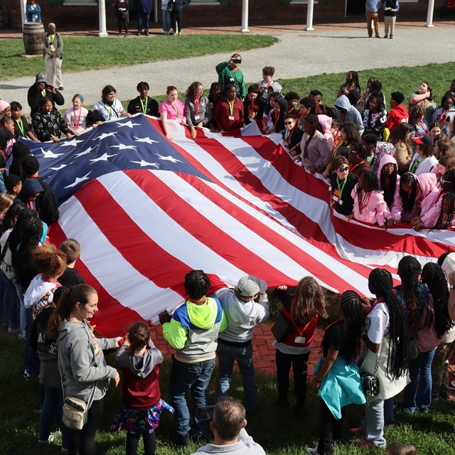 Group of school children assist with folding the garrison flag. 