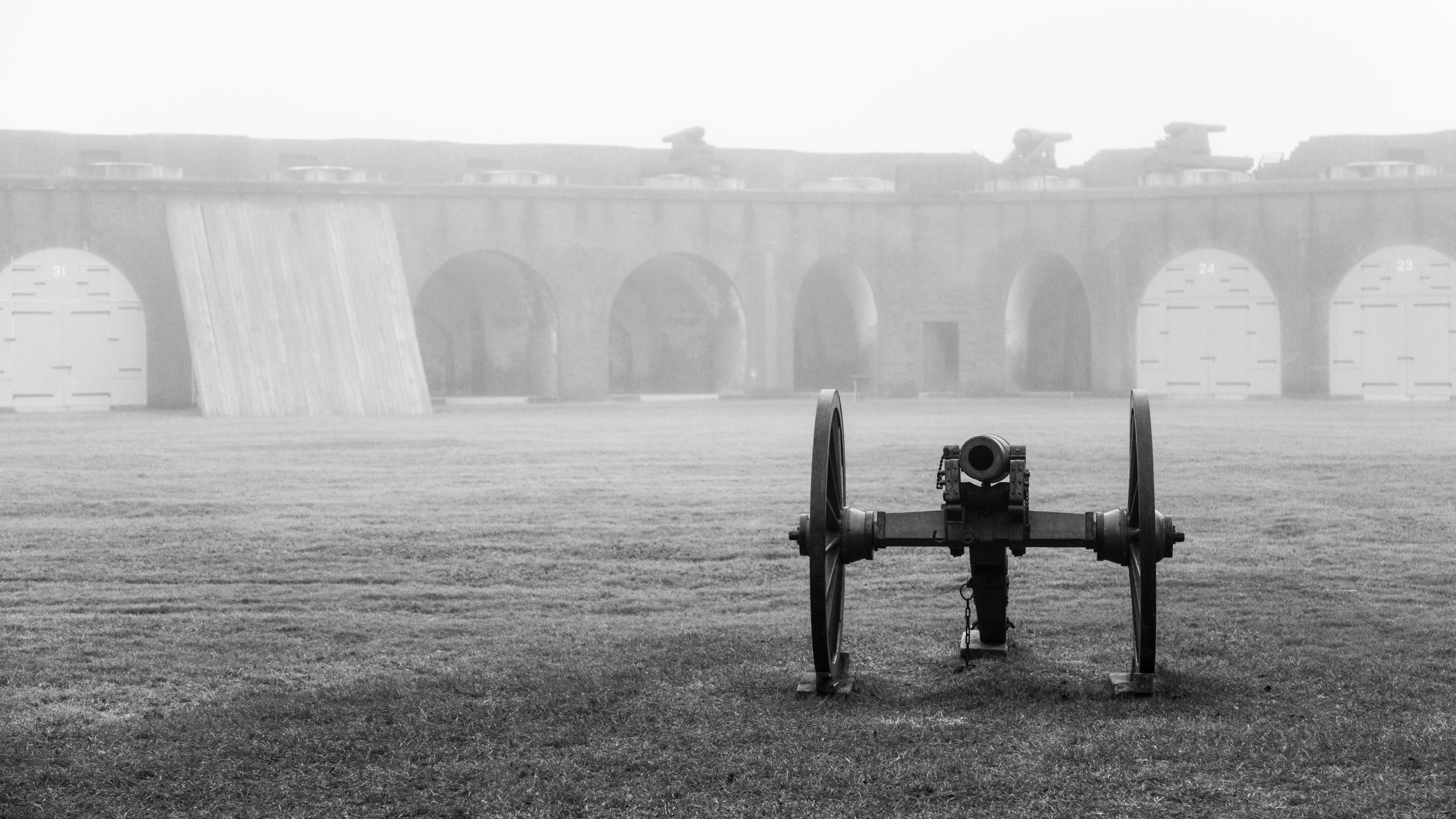 A cannon sits in a foggy parade ground of a fort. 